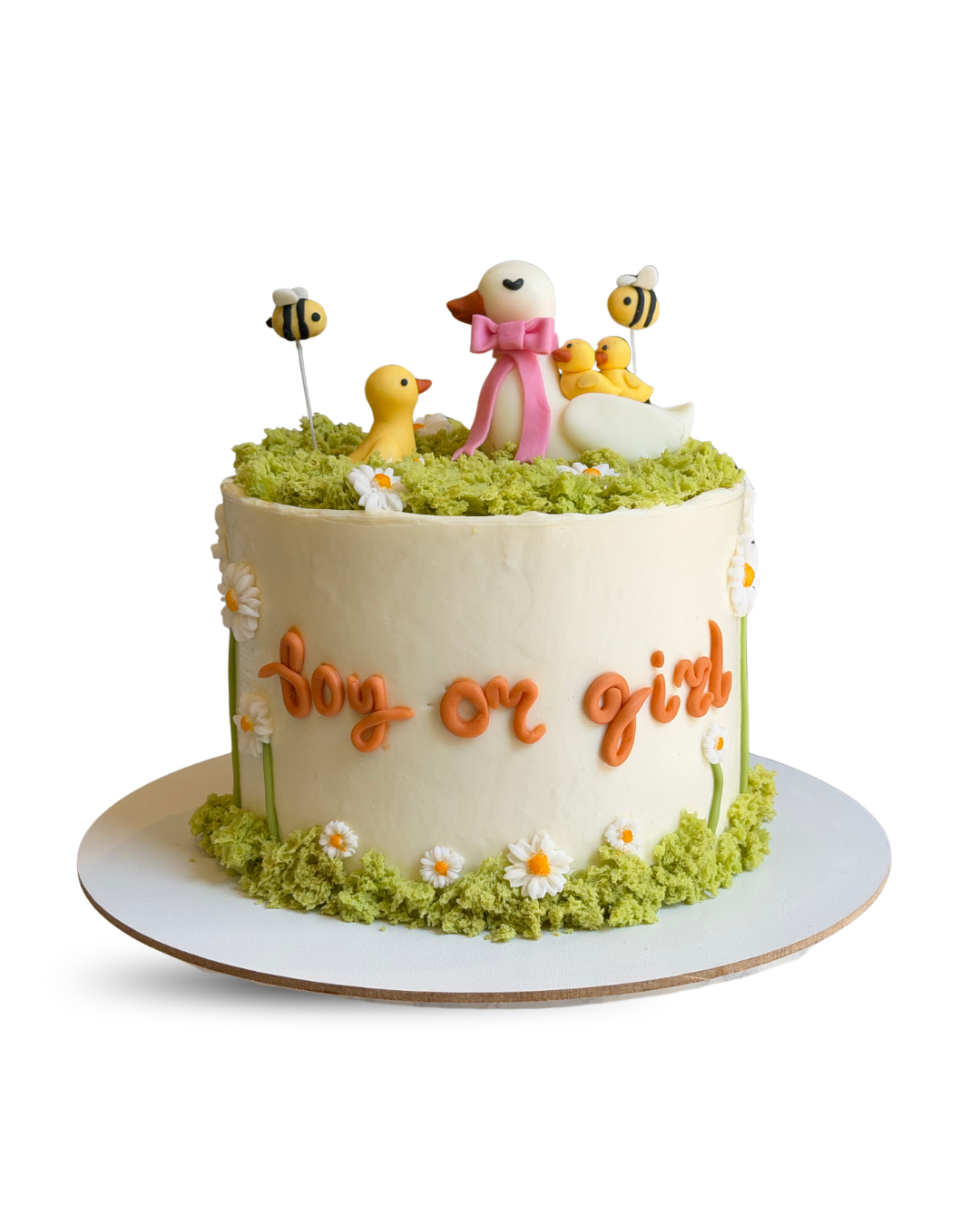 Cream colored cake with Boy or Girl written in orange script, decorated with yellow ducks and bees on green moss frosting by Dessert Boutique.
