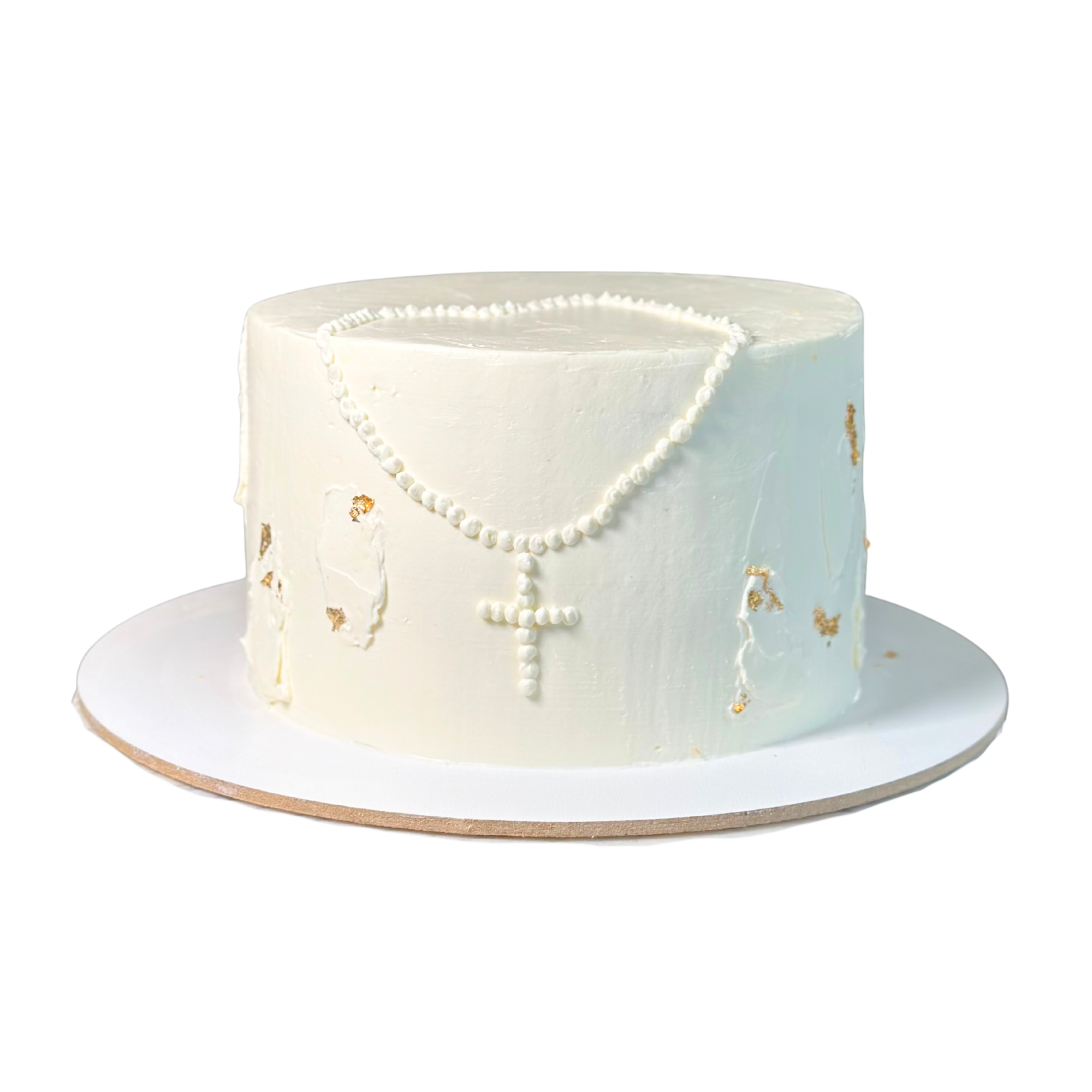 White buttercream cake with a piped pearl cross and gold leaf decorative flakes on the side