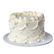 Round white cake featuring multi-layered vintage buttercream piping, ruffled borders, and decorative edible pearls. 