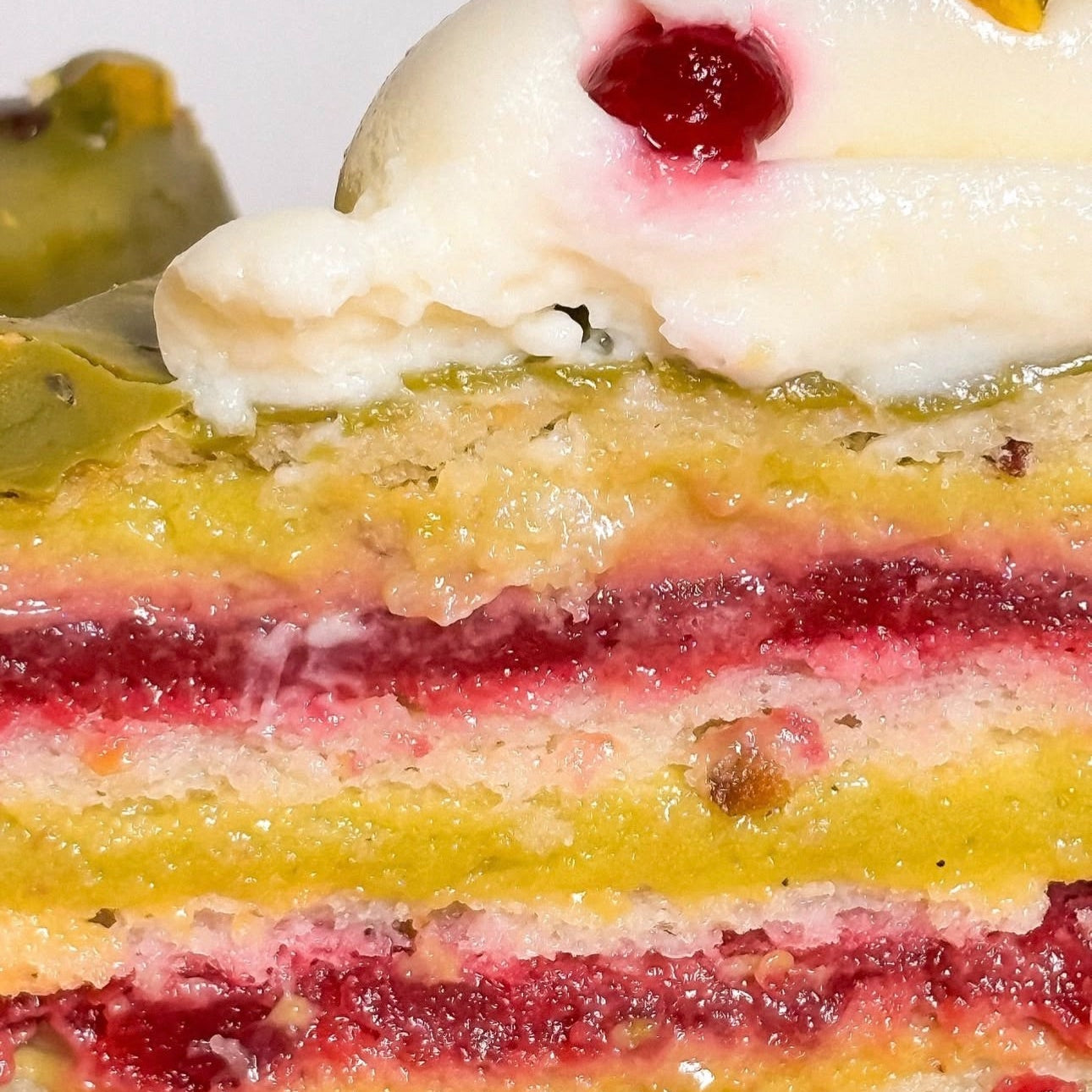 Pistachio and rasberry cake slice with layered filling and cream topping shown whole and cut to show texture