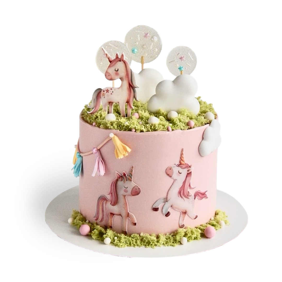 Pink round cake decorated with unicorn cutouts, white clouds, and green moss sponge on top. Dessert Boutique