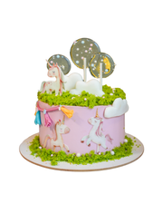 Pink round cake decorated with unicorn cutouts, white clouds, and green moss sponge on top. Dessert Boutique