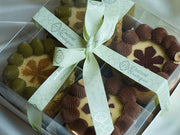 assorted Kyiv cake gift set with classic and pistachio cakes arranged in clear box with a decorative ribbon, labeled 'Dessert Boutique'.