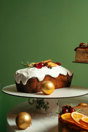 english fruitcake loaf with white icing, dried fruit topping and festive decoration on cake stand