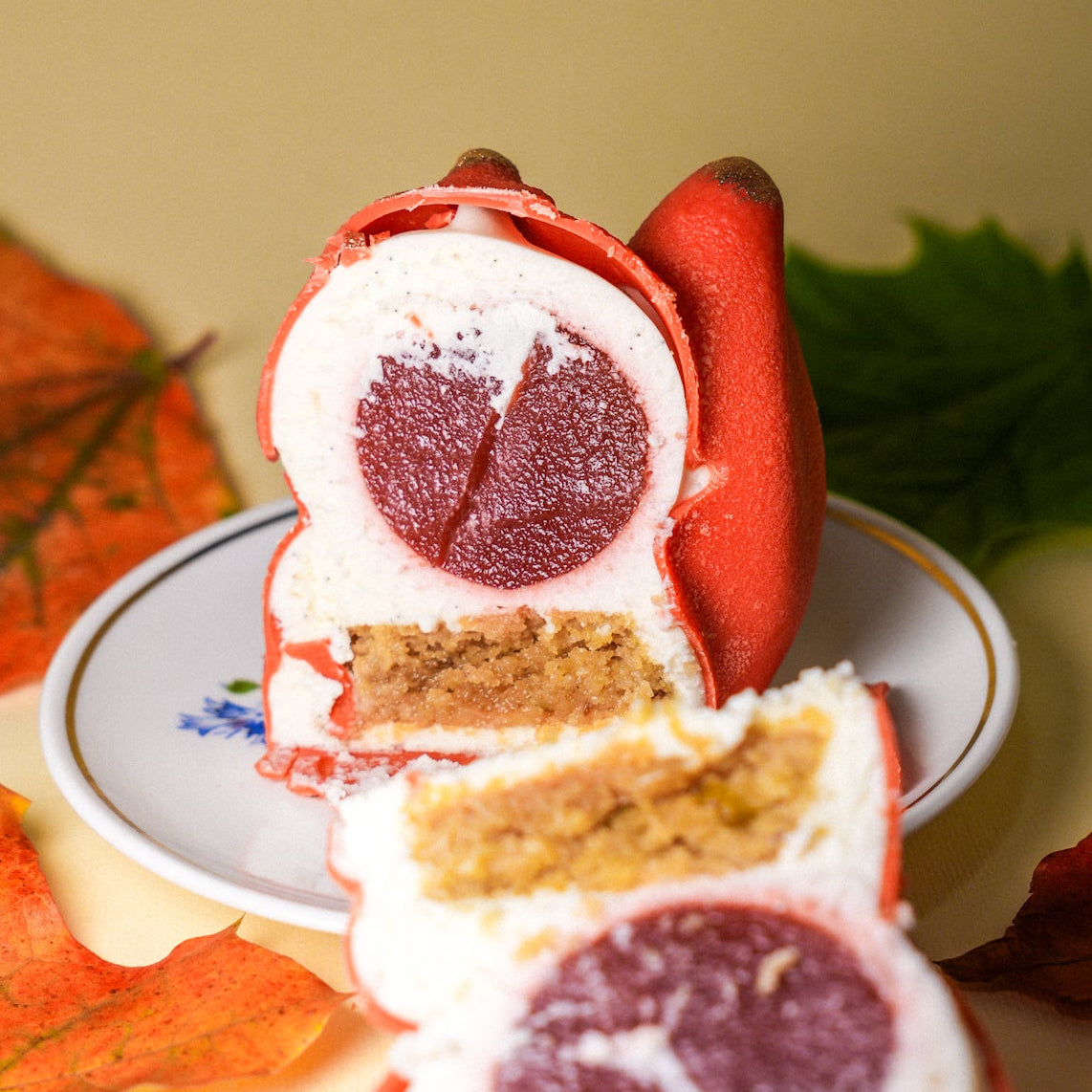 Cross-section of a fox-shaped mousse dessert showing white vanilla mousse, dark red strawberry confit center, and pistachio cookie base