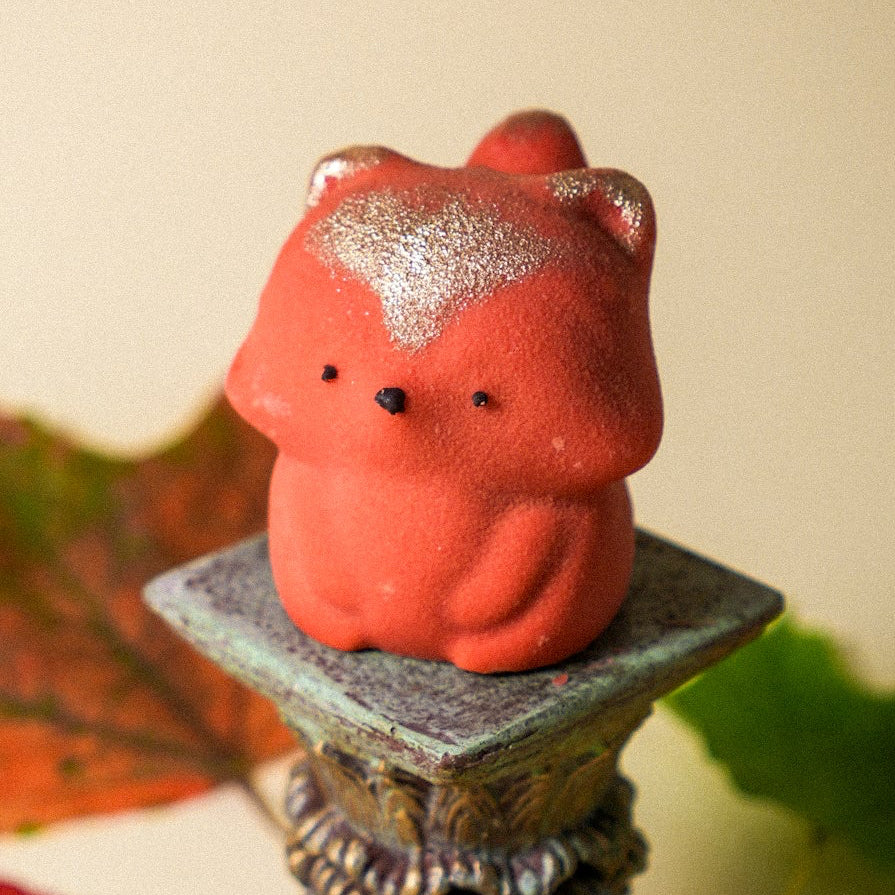 Cute orange fox-shaped mousse dessert with golden shimmer placed on a decorative pedestal with autumn leaves
