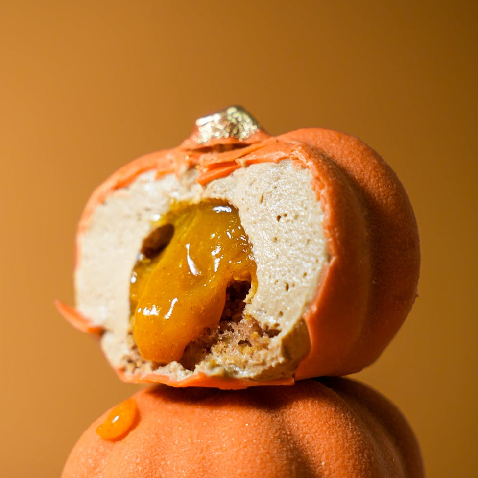 Cut section of a pumpkin-shaped dessert showing the velvety ganache layer, vibrant orange gel center, and spiced sponge base