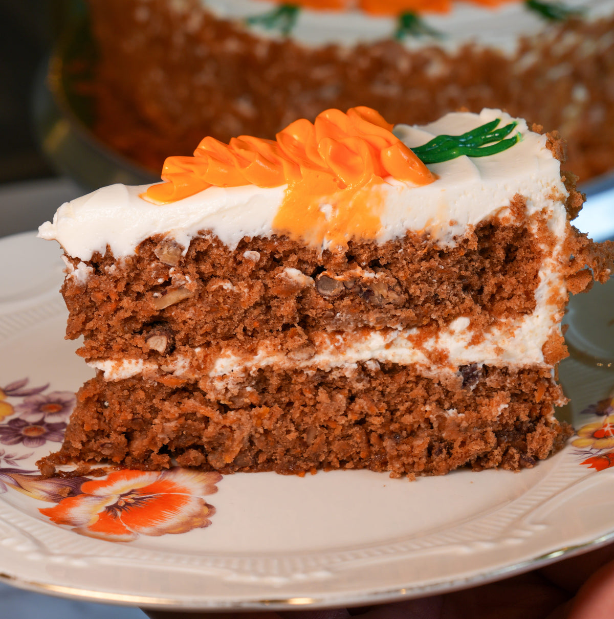 A delicious slice of moist carrot cake showing layers of spiced sponge, pecans, pear, and rich cream cheese frosting.