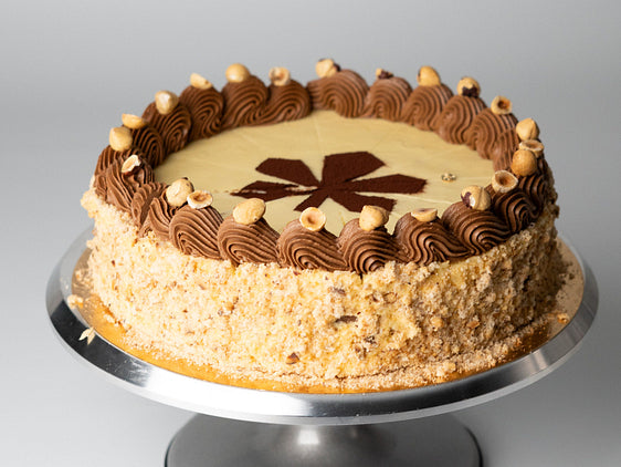 Kyiv cake with hazelnut meringue layers, buttercream piping and nut crumb coating on round cake stand